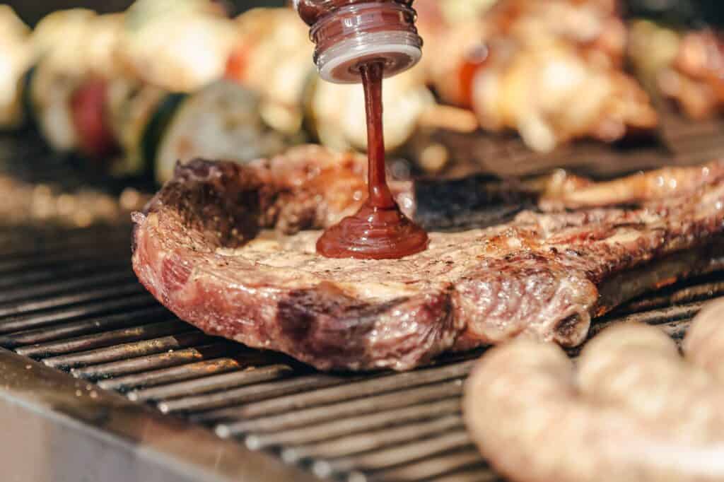 A squirt of unknown sauce atop a grilled steak among a pile of meats during a routine barbecue cook out.