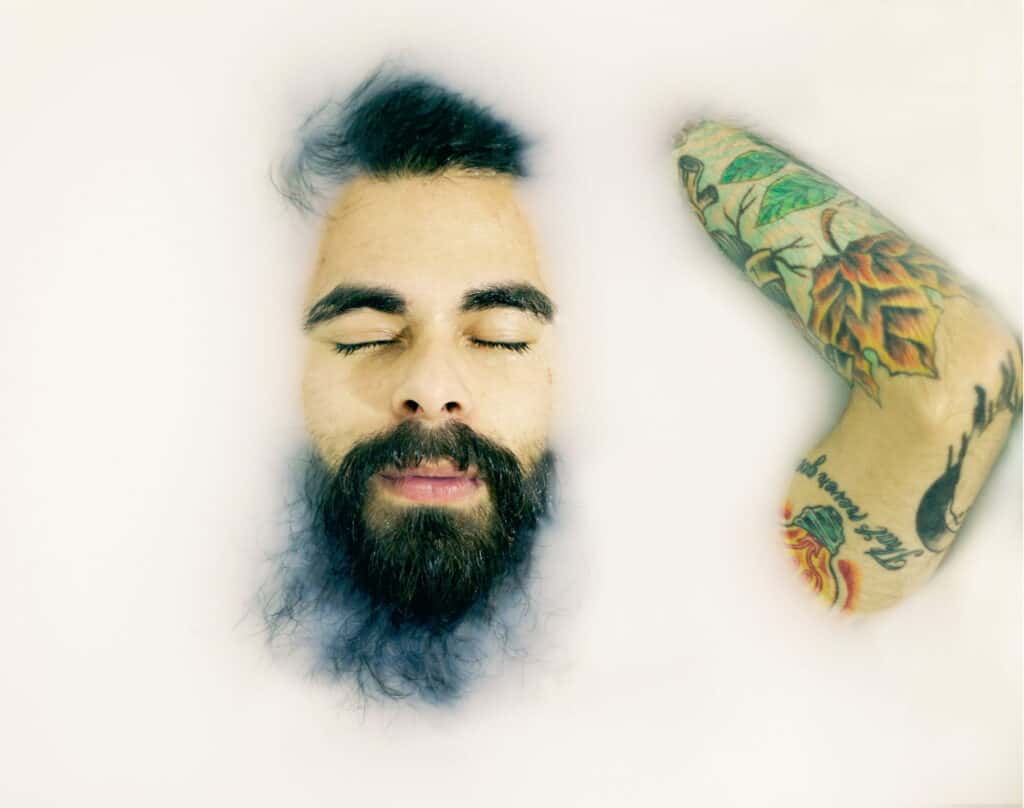 Man resting in bathtub with half his face surfacing with a scruffy beard.