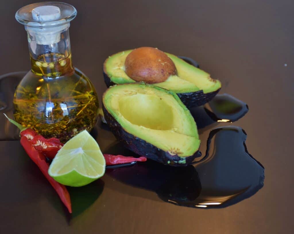 An avocado and a bottle of avocado oil for hair oil treatment.