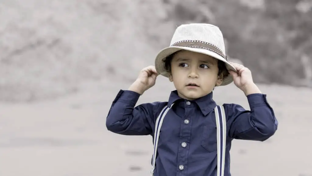 A kid wearing a fedora type hat, pulling the hat down on him a little.