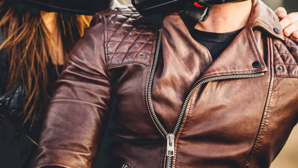 Closeup of a couple wearing leather jackets on a motorcycle.
